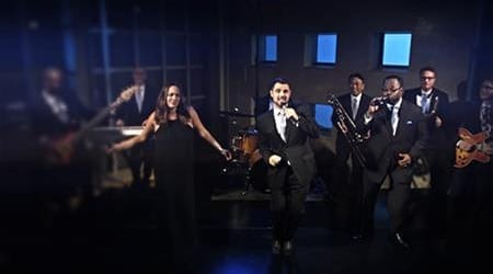A Boston Band performs on stage with multiple musicians, including vocalists, guitarists, a trumpet player, and a drummer in formal attire—perfect for unforgettable wedding music.
