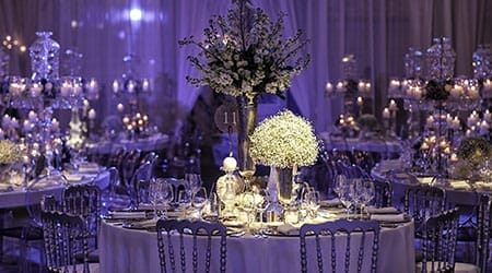 Elegant banquet hall with round tables set for an event, decorated with white flowers, glassware, and lit candles, creating a sophisticated atmosphere perfect for enjoying live Wedding Music or a Boston Band.