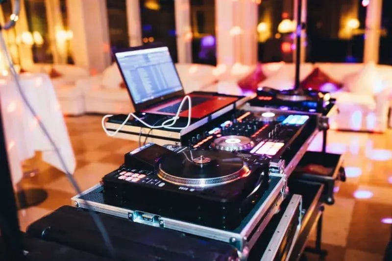 A DJ booth setup with a laptop, turntable, and mixer, illuminated by colorful party lights in a lounge or event space—perfect for Boston Band events or unforgettable wedding music celebrations.